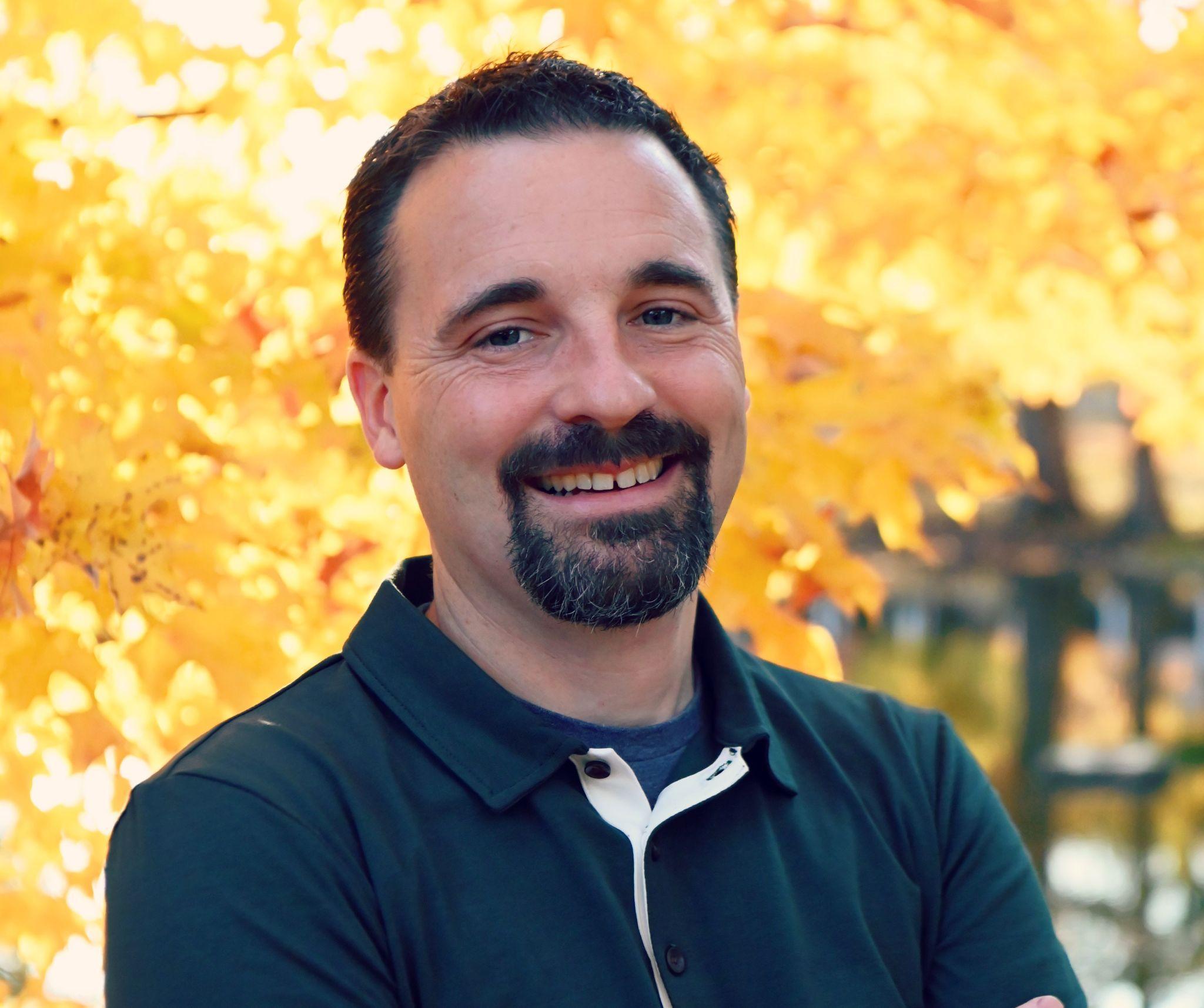 Matthew, counselor at Rooted Counseling Ohio, smiling outdoors in front of autumn leaves